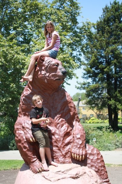 A boy and a girl posing for a picture with a large statue of a giant sloth from the Ice Age